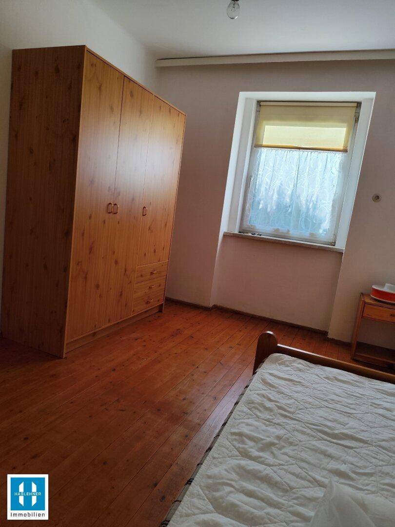 Schlafzimmer mit Holzdielenboden, großem Holzschrank und schrägem Dachfenster für natürliches Licht.