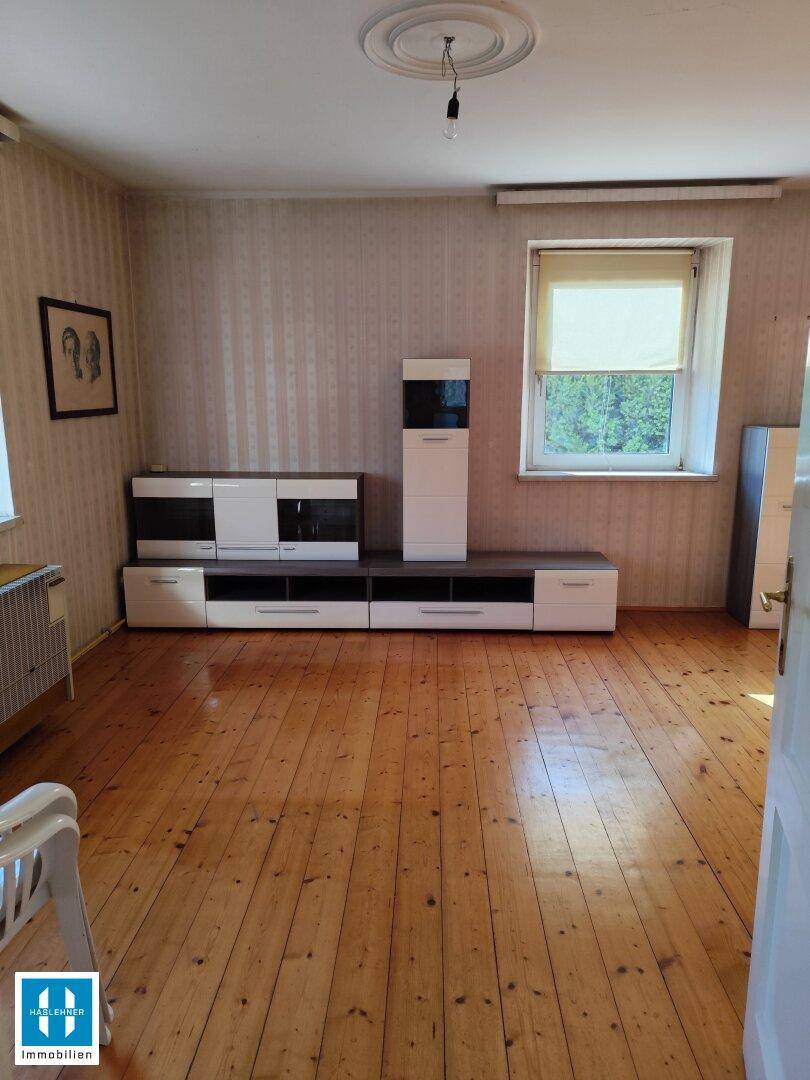 Geräumiges Wohnzimmer mit Holzdielenboden, moderner Medienwand und dekorativer Stuckdecke.
