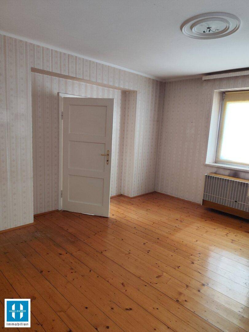 Helles Zimmer mit Holzdielenboden, Tapeten und Heizkörper, ideal als Wohn- oder Essbereich nutzbar.