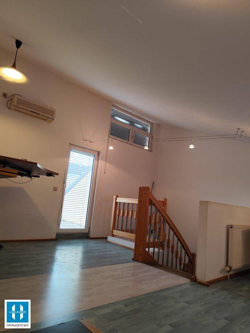 Heller Innenraum mit Dachschräge, Laminatboden und Klimaanlage, mit Blick auf eine Holztreppe.
