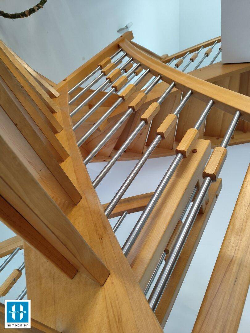 Detailansicht einer modernen Holztreppe mit eleganten Metallstäben und geschwungenem Geländer.