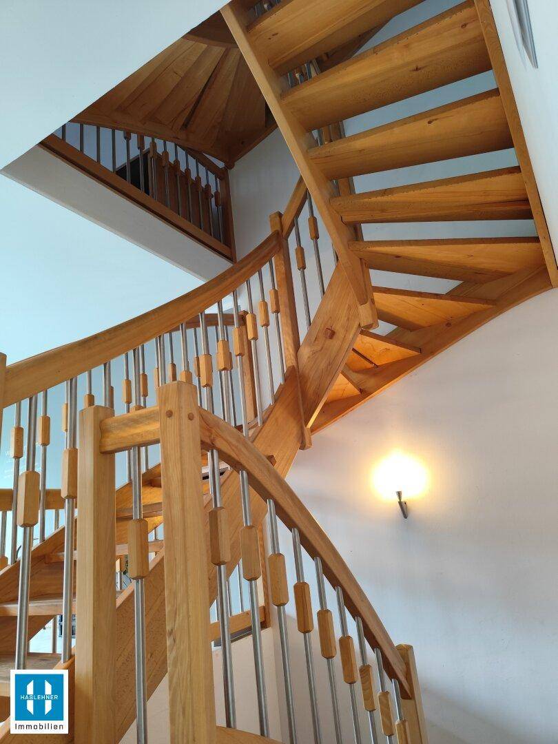 Geschwungene Holztreppe mit Metallgeländer, die verschiedene Ebenen des Hauses verbindet.
