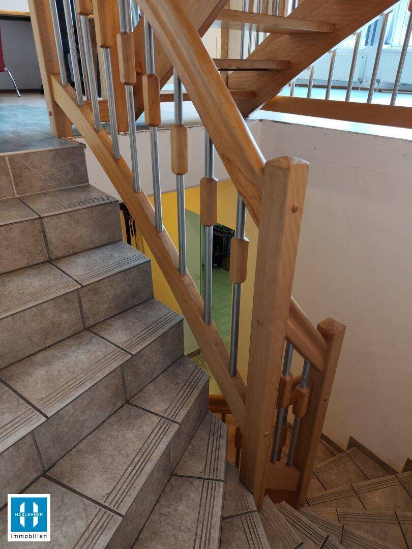 Geflieste Treppe mit Holzgeländer und Metallstäben, die zu den oberen Etagen führt.