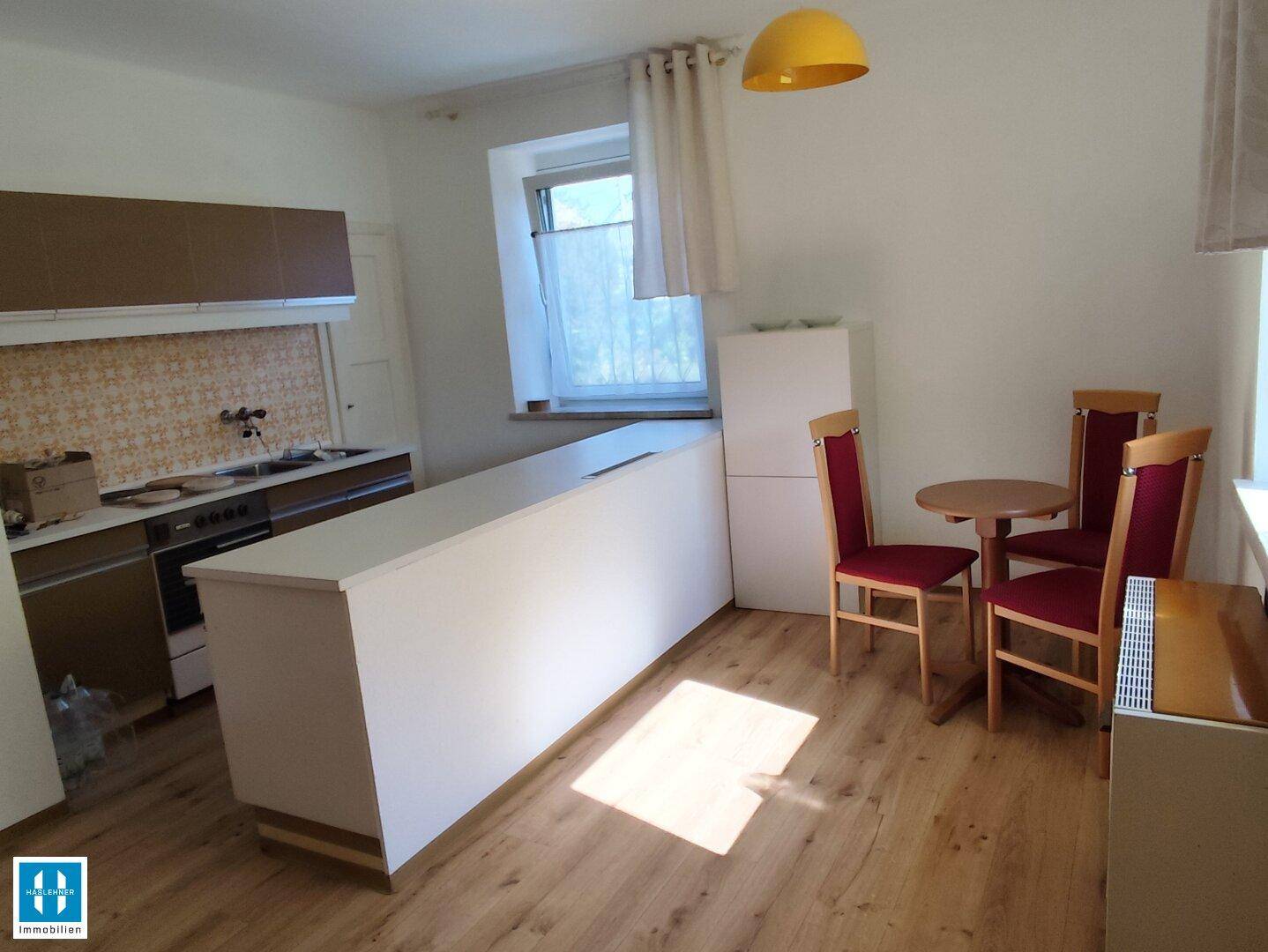 Offene Küche mit Kücheninsel, Essbereich und Holzboden, beleuchtet durch ein Fenster.