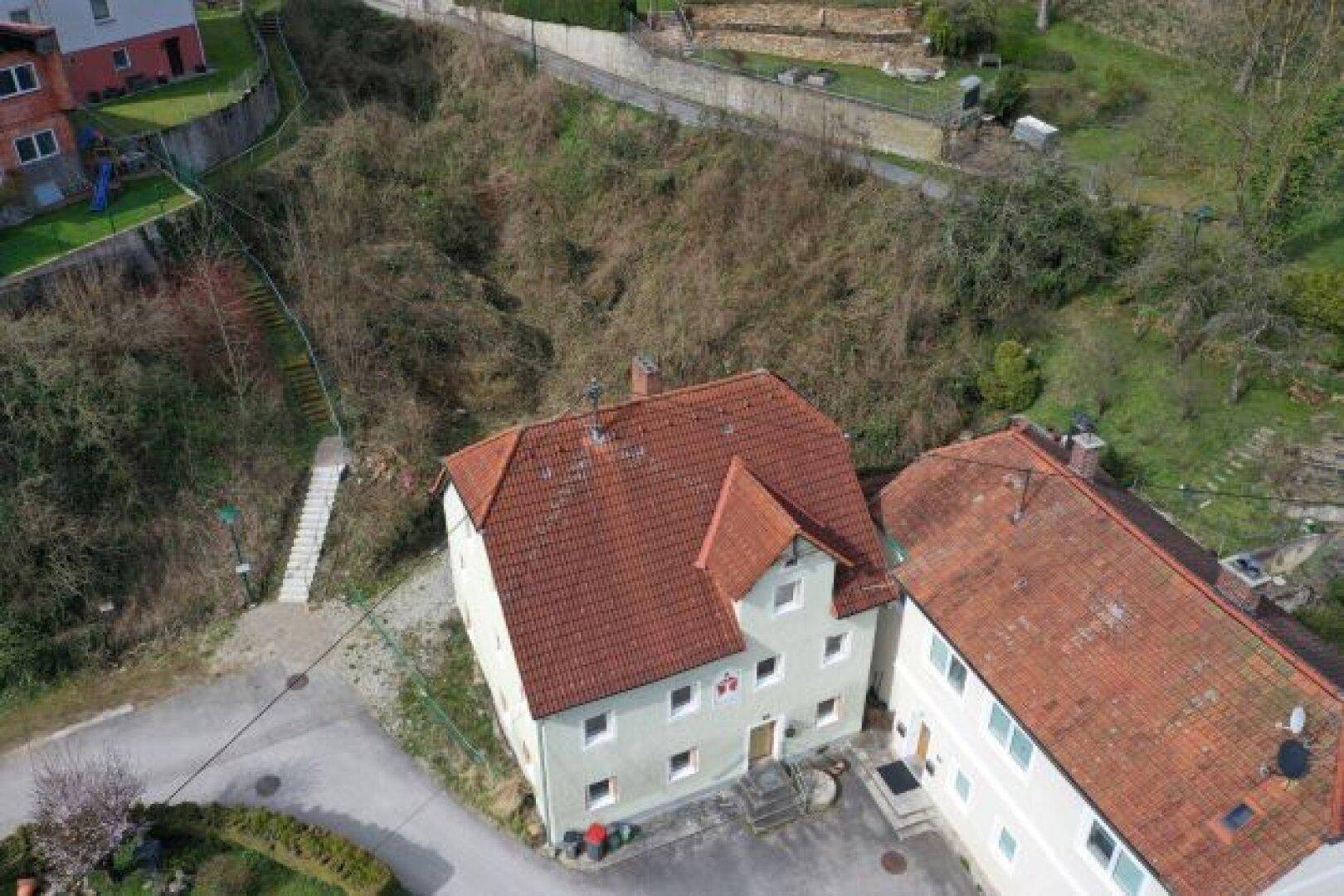 Vogelperspektive des Hauses mit rotem Ziegeldach und dem angrenzenden Hanggrundstück.
