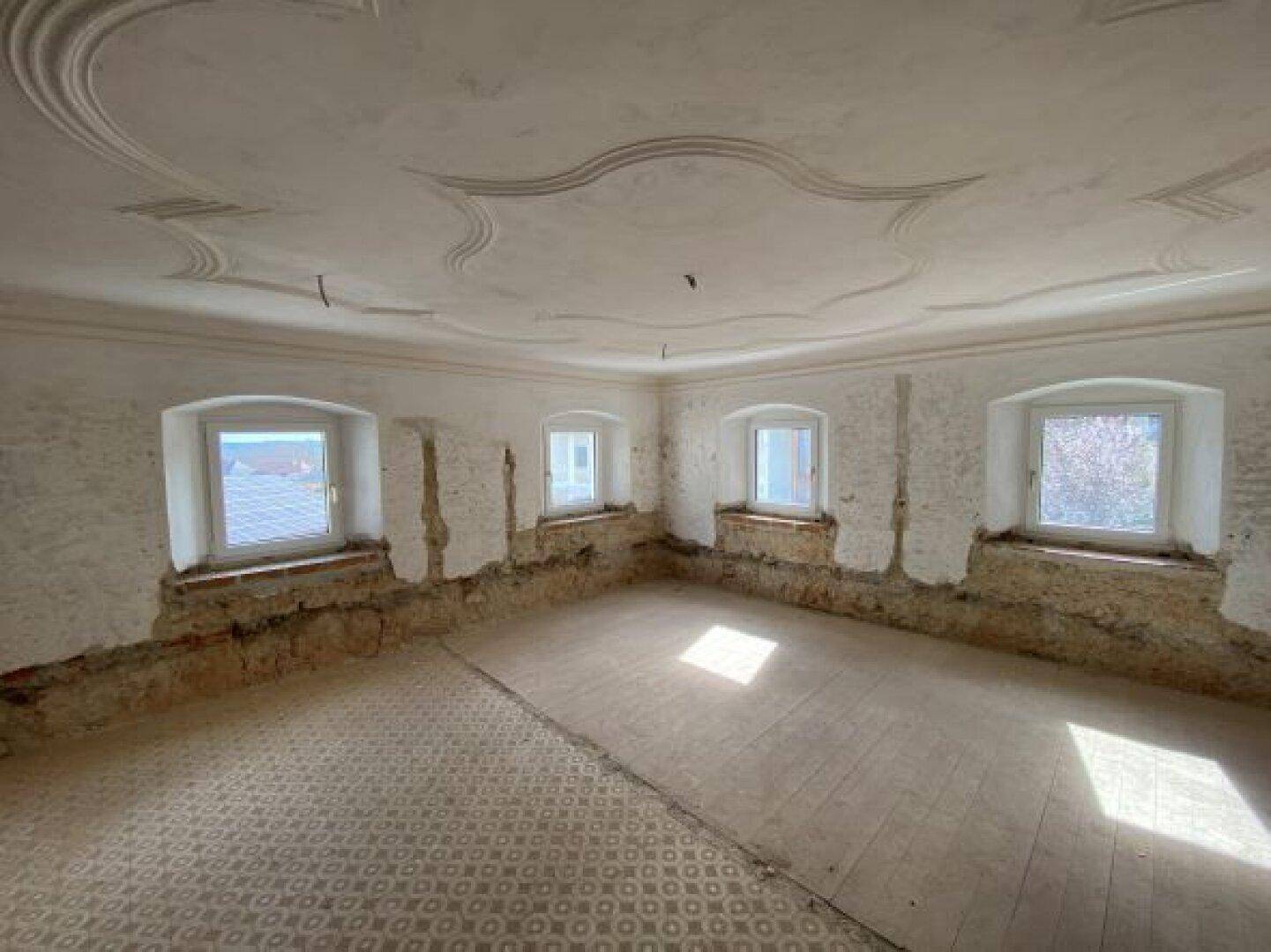 Raum im Rohbau mit Stuckdecke und freigelegten Wänden, bereit für die Renovierung.