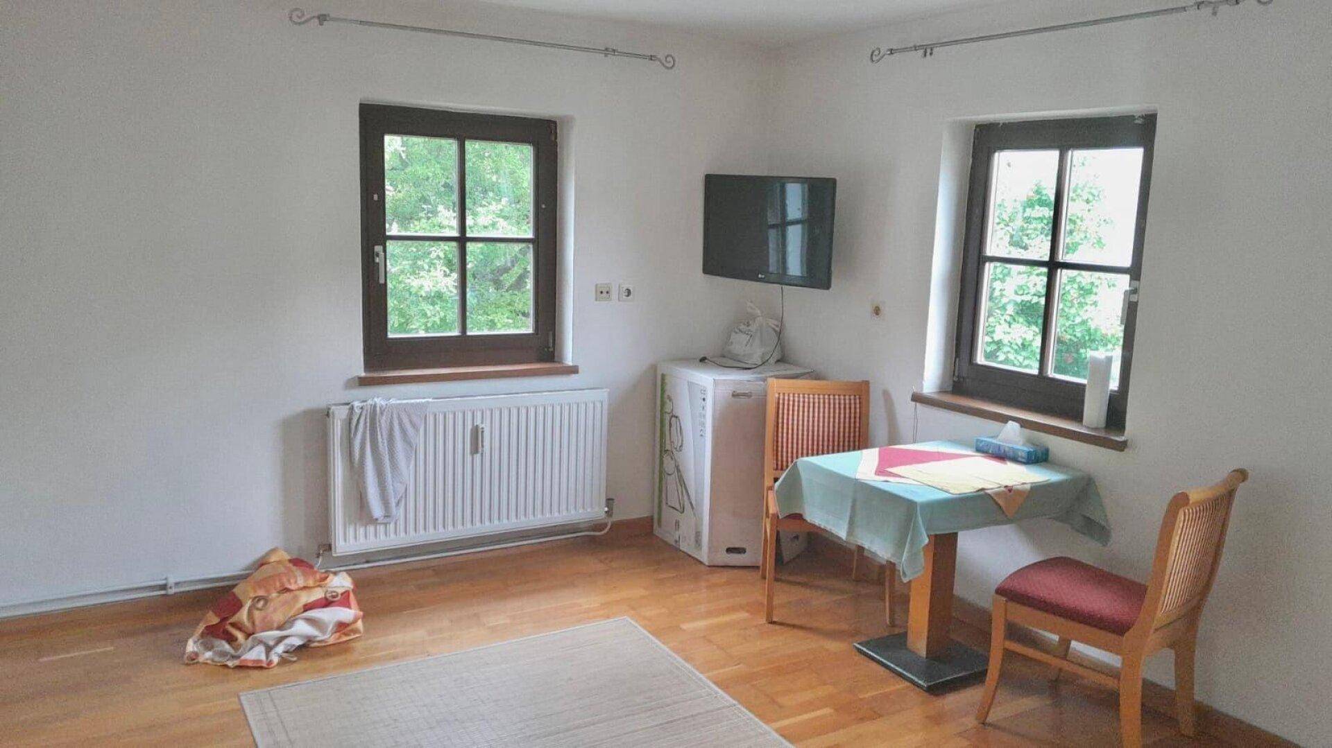 Heller Raum mit zwei Fenstern, kleinem Tisch und Stühlen, bietet viel Tageslicht.