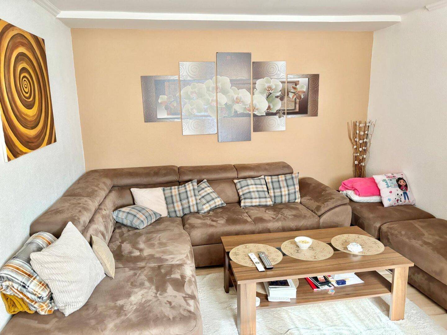 Gemütliches Wohnzimmer mit großem Ecksofa, Couchtisch und dekorativen Bildern an der Wand.