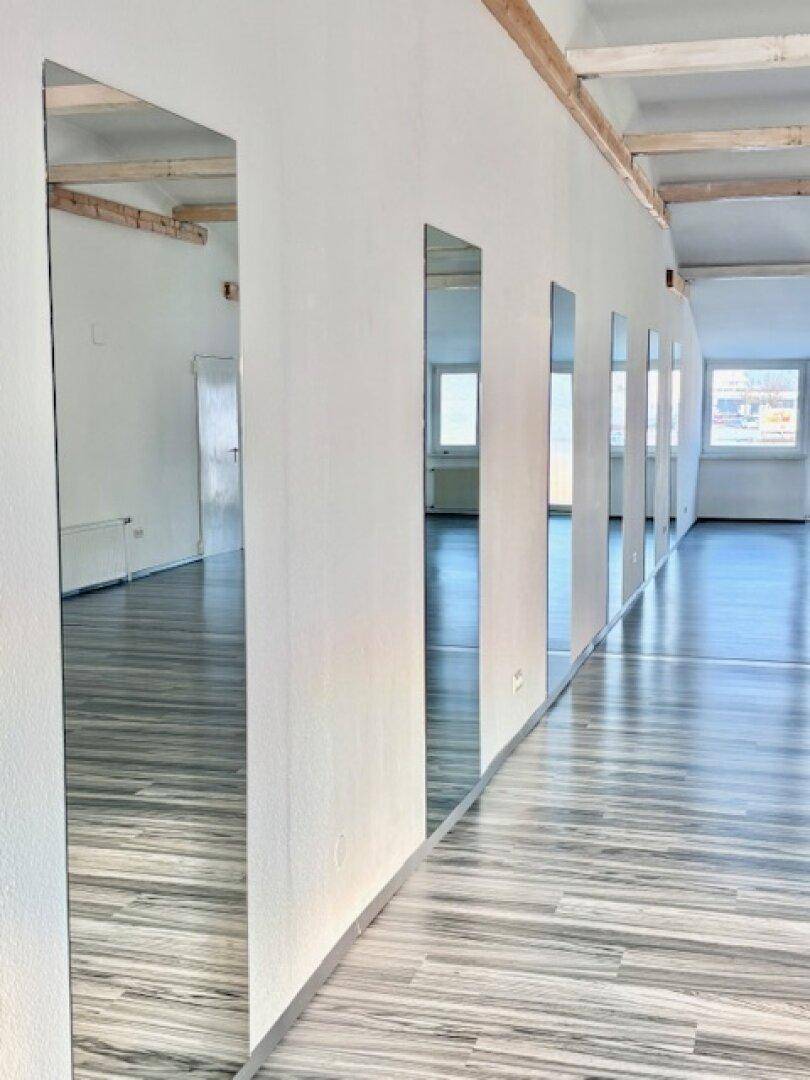 Spiegelwand in einem hellen Gewerberaum mit Holzdeckenbalken und glänzendem Laminatboden.