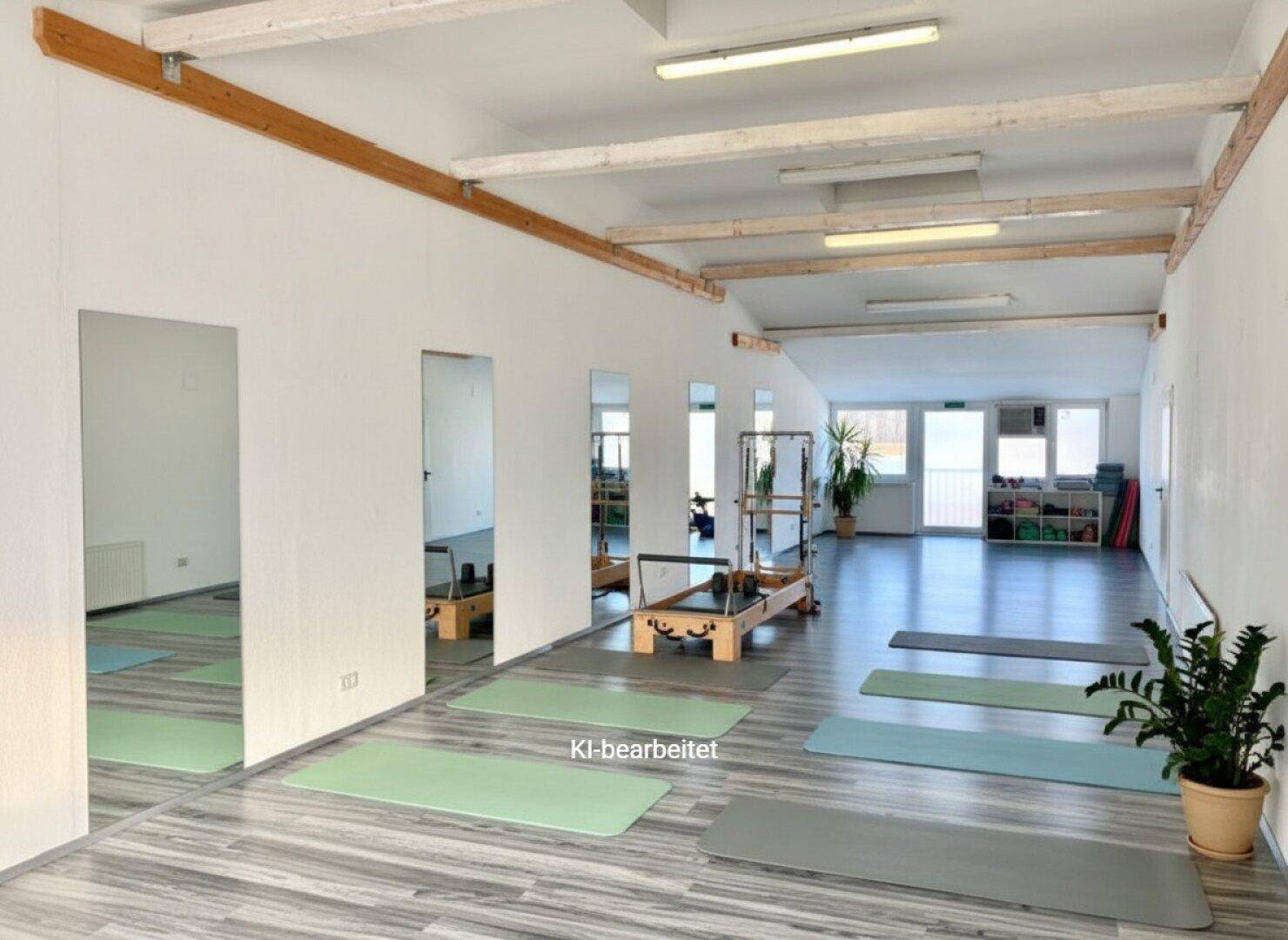 Heller Gewerberaum mit Pilates-Geräten, Spiegelfronten und Holzdeckenbalken, gut beleuchtet.