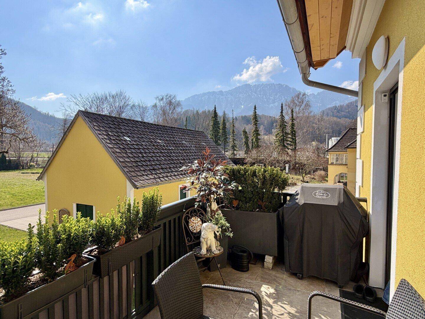 Sonniger Balkon mit Grill und Pflanzen, bietet einen weiten Blick auf die umliegenden Berge.