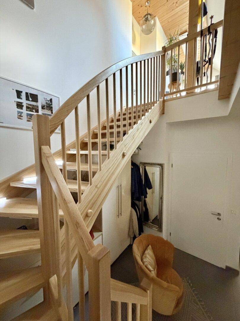 Helles Treppenhaus mit Holztreppe und Geländer, führt zu den oberen Etagen des Hauses.