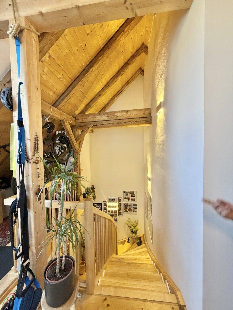 Holztreppe mit offenem Geländer und sichtbaren Holzbalken, die zu einem oberen Bereich führt.