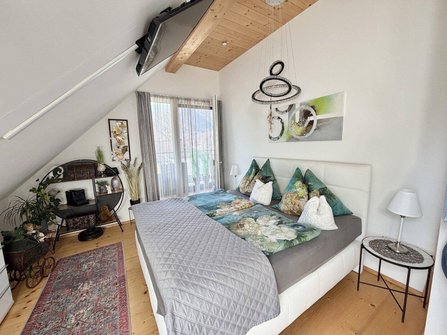 Gemütliches Schlafzimmer mit Holzbalkendecke, Doppelbett und Zugang zu einem Balkon.