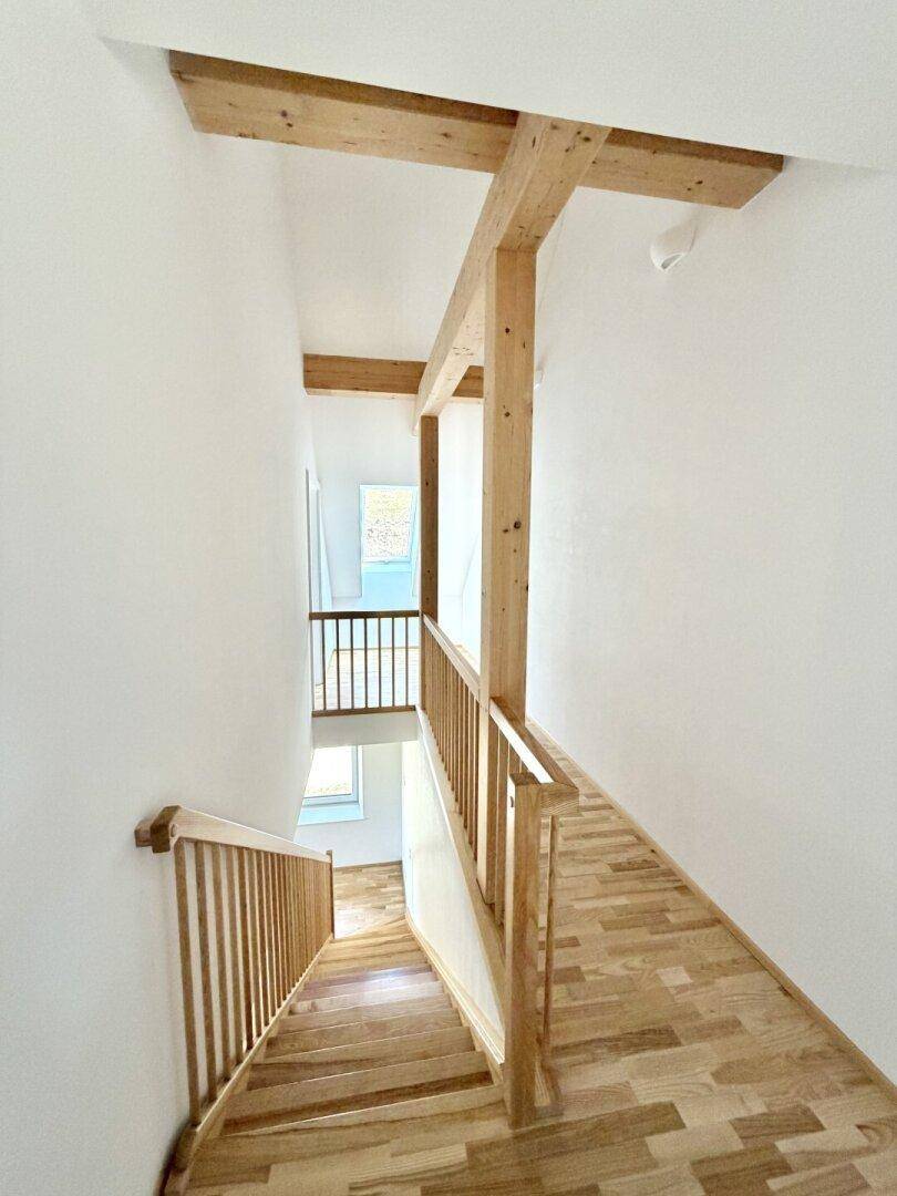Helles Treppenhaus mit Holzstufen und Geländer, das zu einem oberen Stockwerk führt.