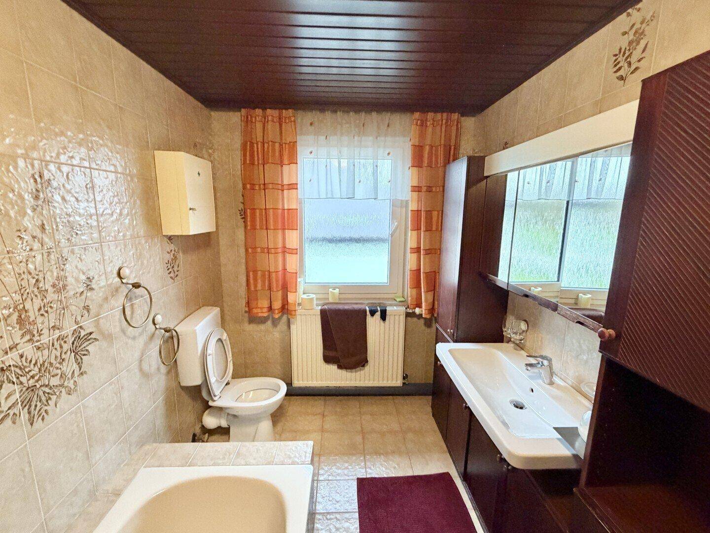 Badezimmer im Stil der 80er Jahre mit Badewanne, WC und Fenster.
