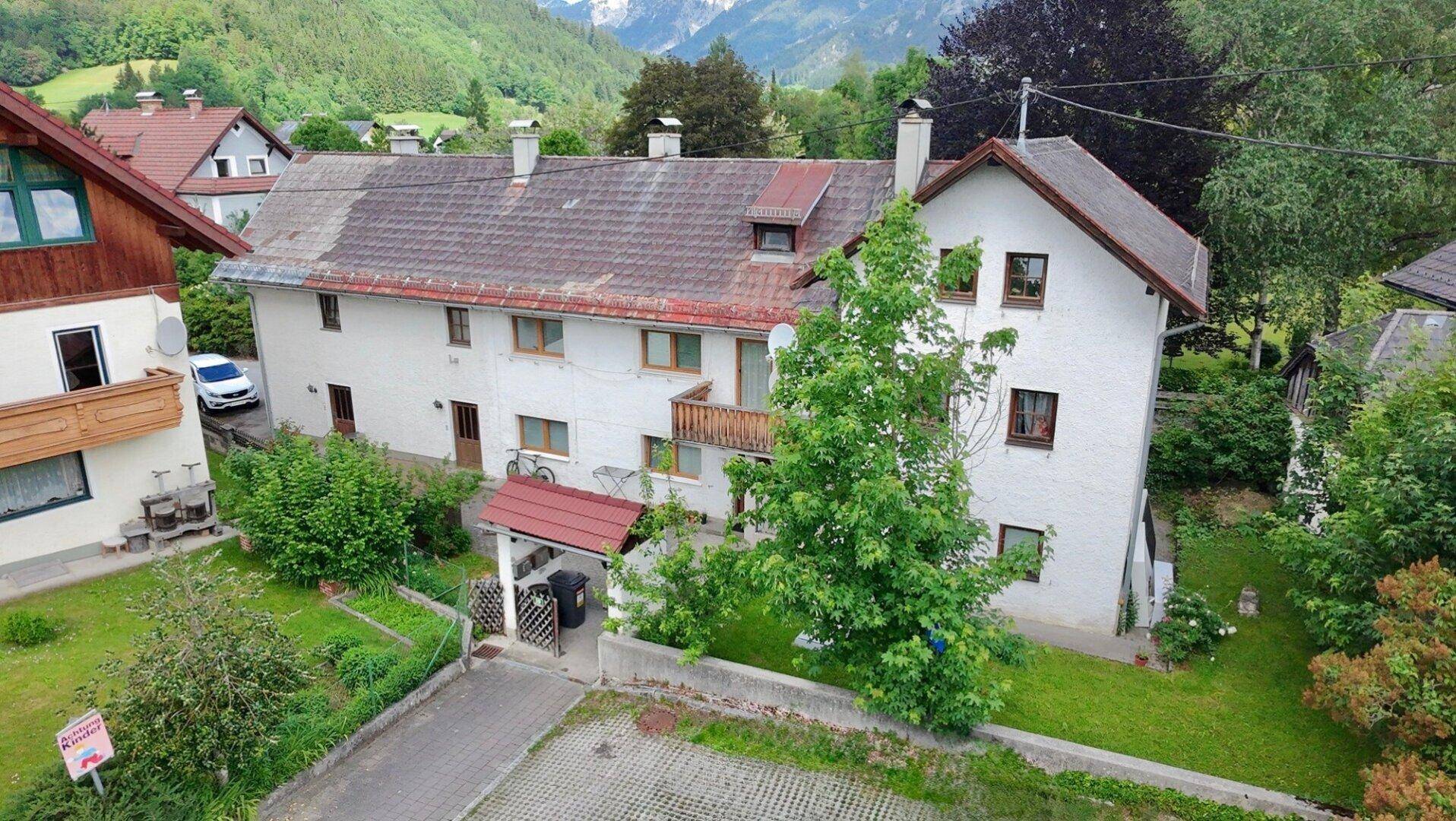 Gesamtansicht des Hauses mit Balkonen, Gartenbereich und beeindruckender Bergkulisse im Hintergrund.
