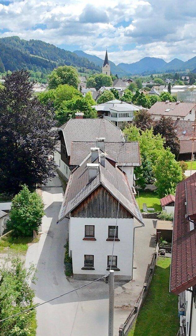 Blick auf das Gebäude mit traditionellem Dach und einer weiten Aussicht auf das Dorf und die Berge.