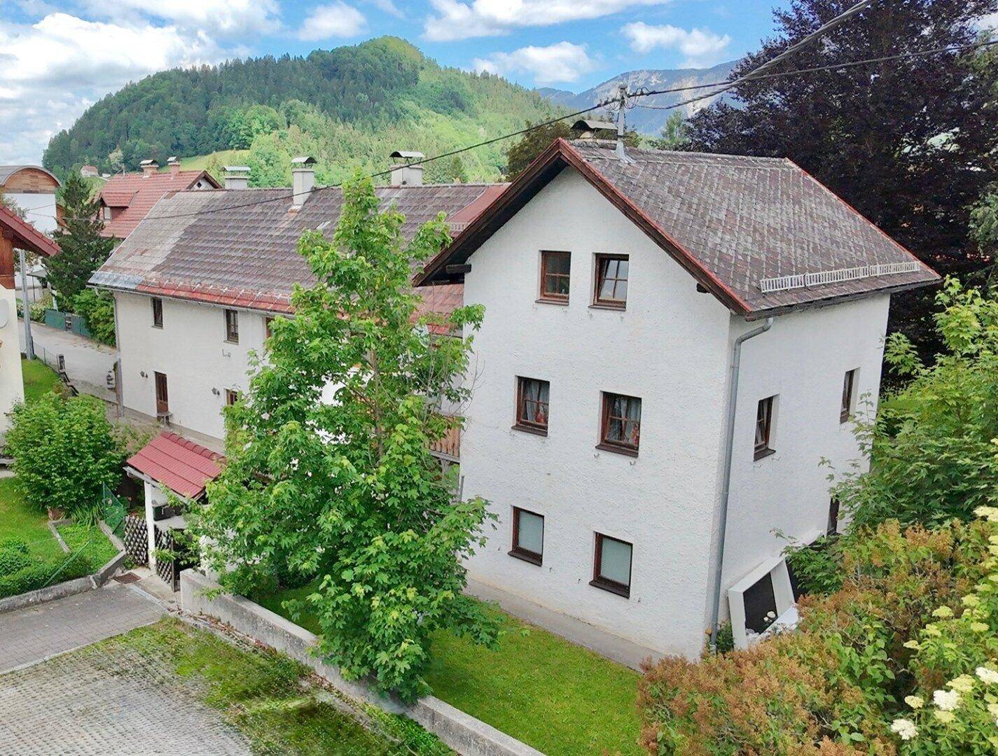 Das gepflegte Gebäude mit weißer Fassade und Satteldach, eingebettet in eine grüne Landschaft.