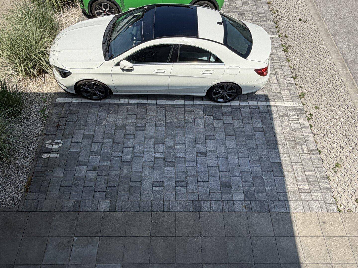 Außenparkplatz mit Pflastersteinen und einem weißen Auto unter strahlendem Sonnenschein.