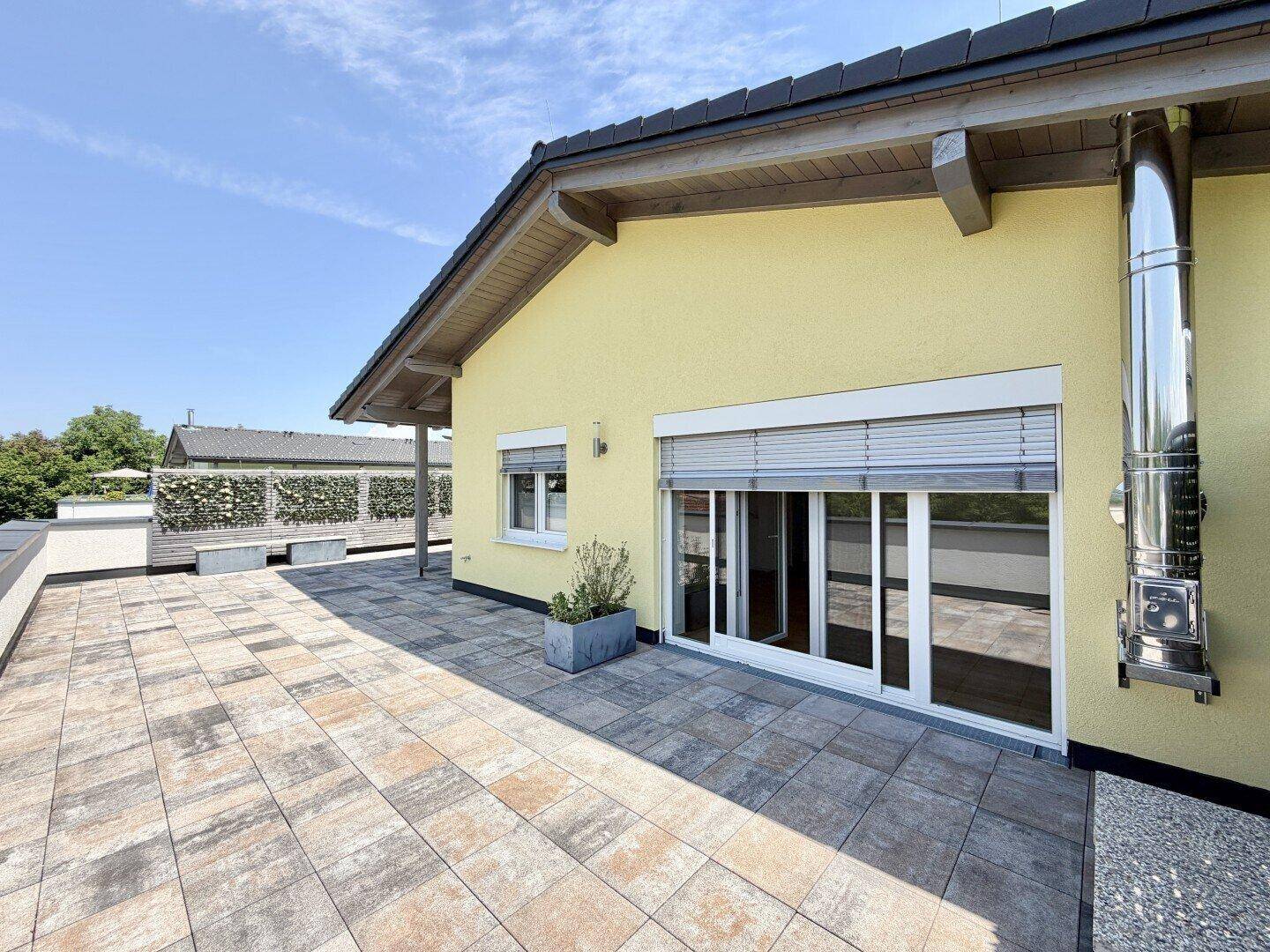 Große Sonnenterrasse mit gelber Fassade, Rollläden und einem externen Edelstahlkamin.