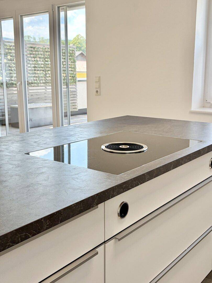 Detailaufnahme der Kücheninsel mit integriertem Induktionskochfeld und dunkler Arbeitsplatte.