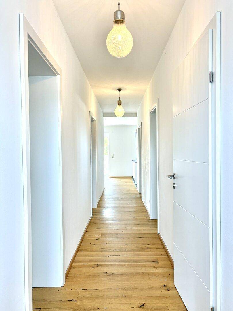 Heller Flur mit Holzboden und mehreren weißen Türen, der in die Tiefe des Hauses führt.