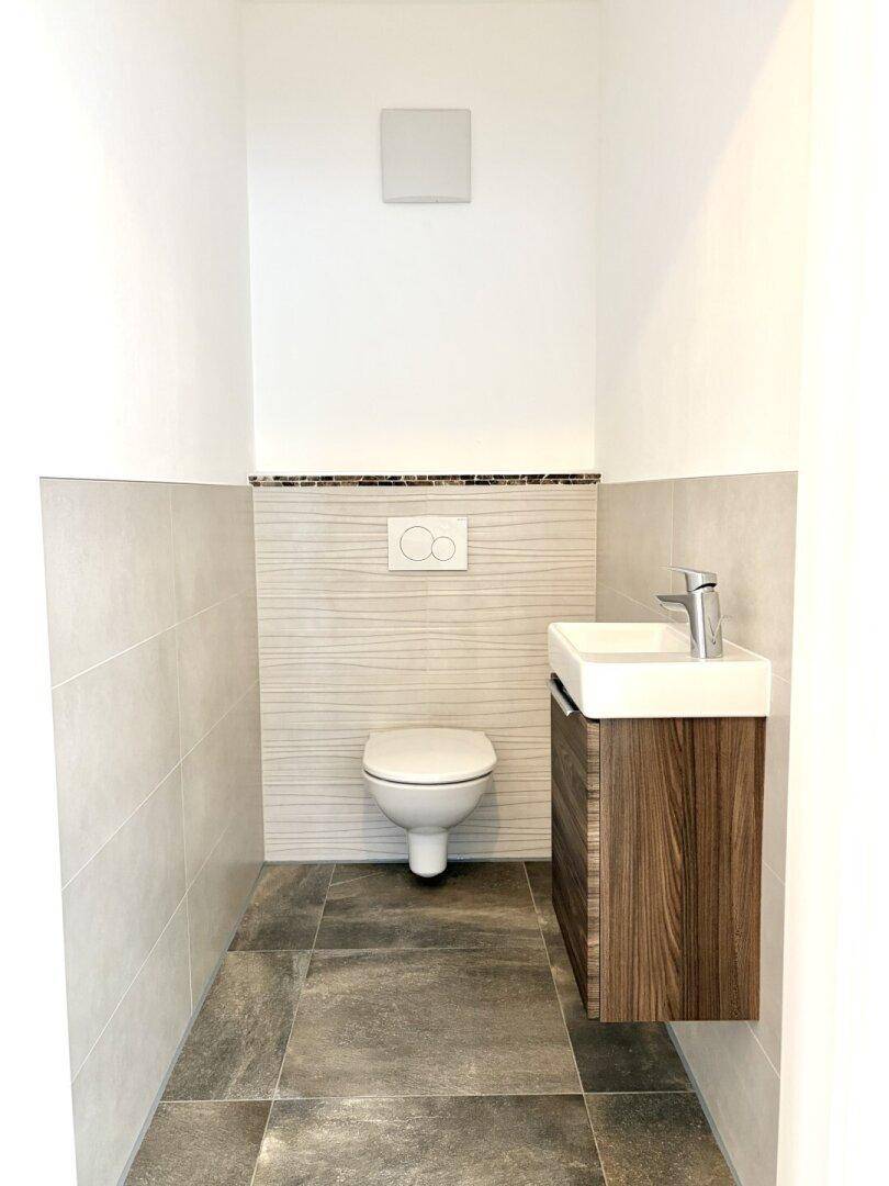 Kleines Gäste-WC mit wandhängender Toilette, modernem Waschbecken und grauen Fliesen.