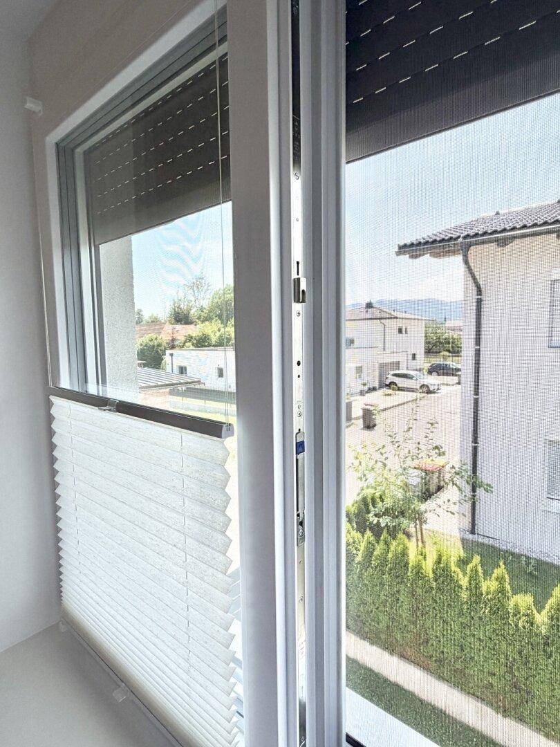 Fenster mit Plissee und Rollladen, das einen Blick auf die Nachbarschaft freigibt.