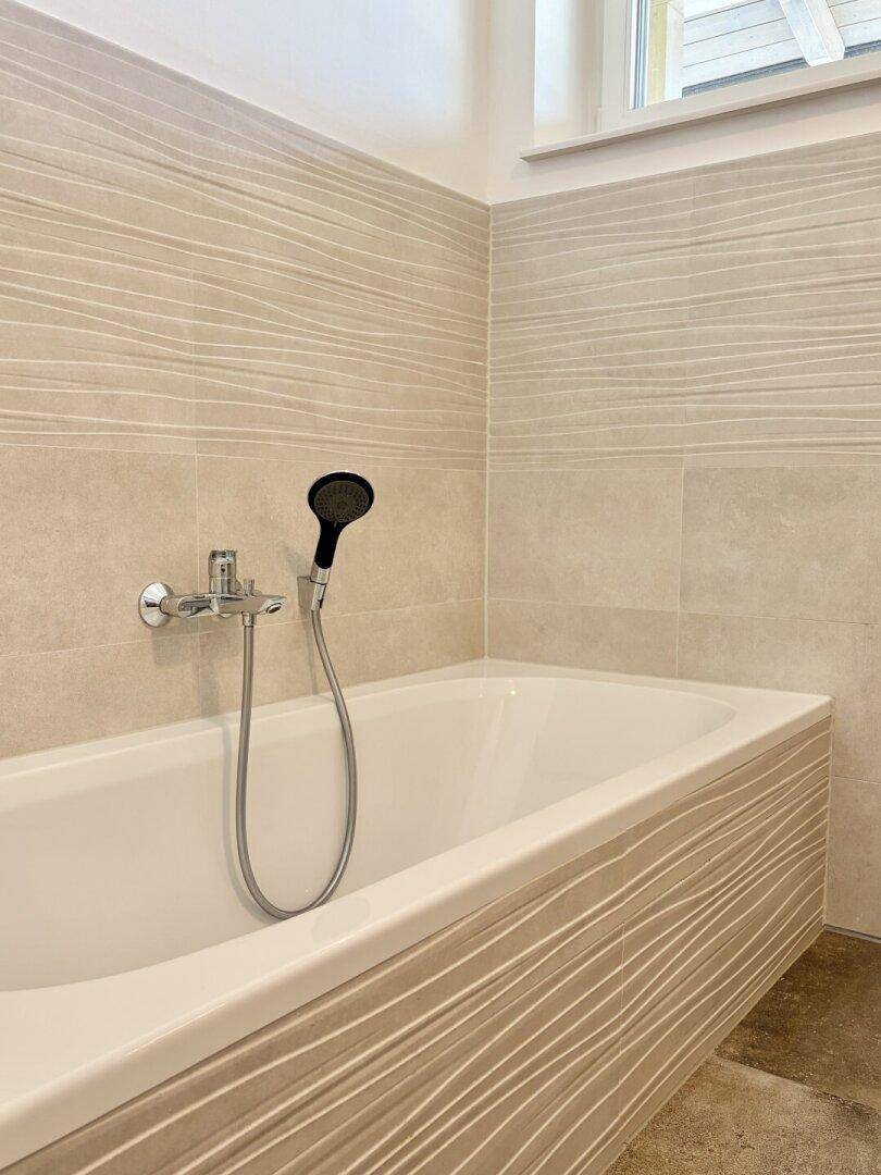 Badewanne mit moderner Armatur und beigefarbenen Fliesen mit Wellenstruktur im Badezimmer.