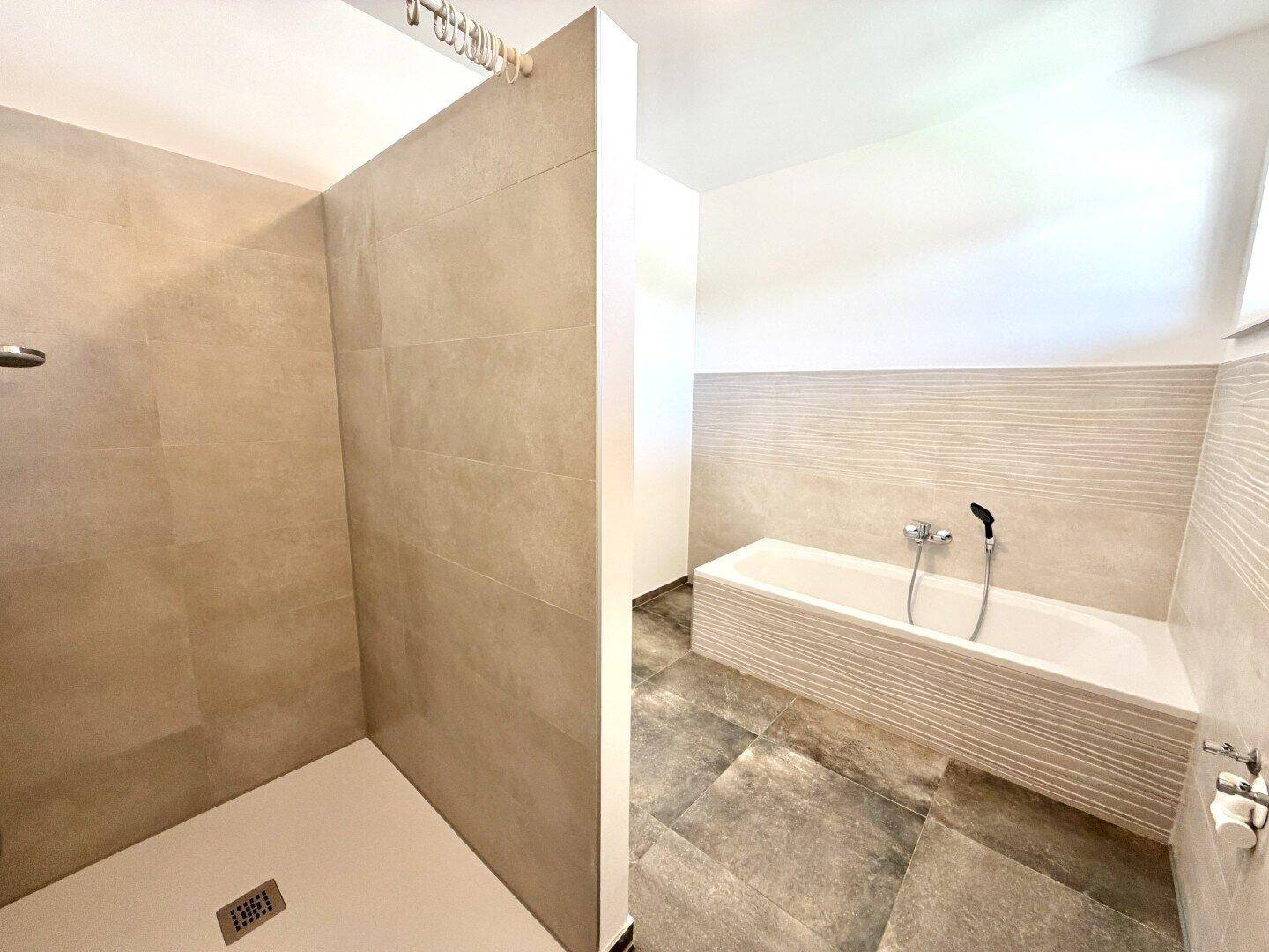 Modernes Badezimmer mit begehbarer Dusche, Badewanne und großformatigen Fliesen in Grautönen.
