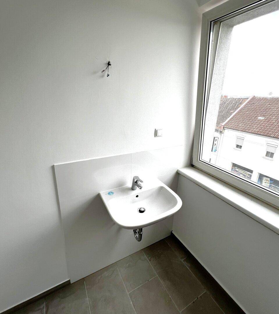 Kleines WC mit Waschbecken, Fenster und Fliesenboden, hell und funktional gestaltet.