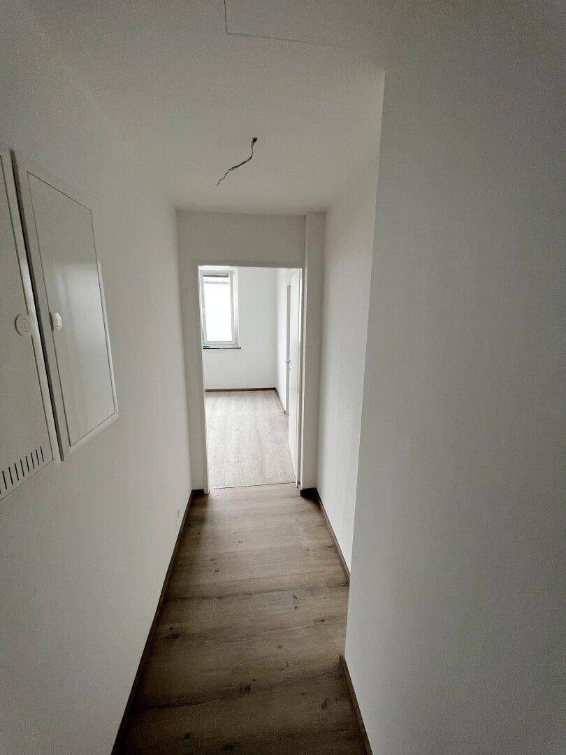 Langer, leerer Flur mit hellem Holzboden und weißen Wänden, der zu weiteren Räumen führt.