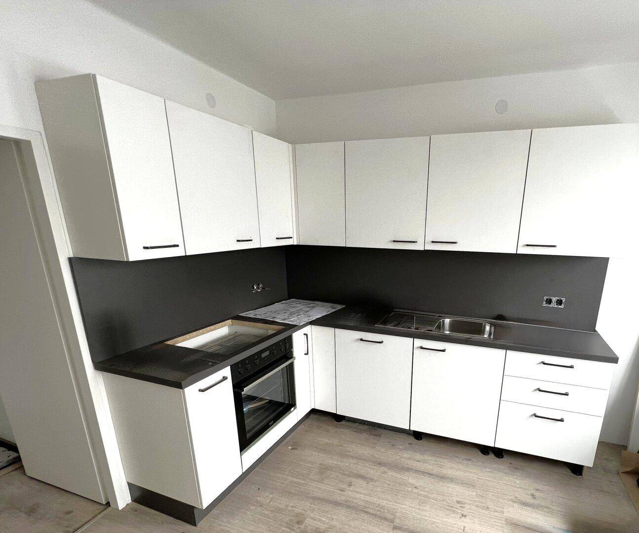 Neue, moderne Küche mit weißen Schränken, dunkler Arbeitsplatte und integriertem Backofen.