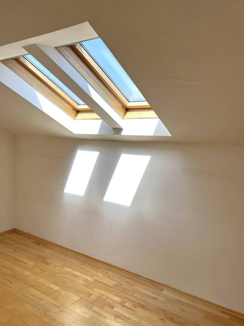 Heller Raum mit Holzboden und mehreren Dachfenstern, die viel Tageslicht hereinlassen.