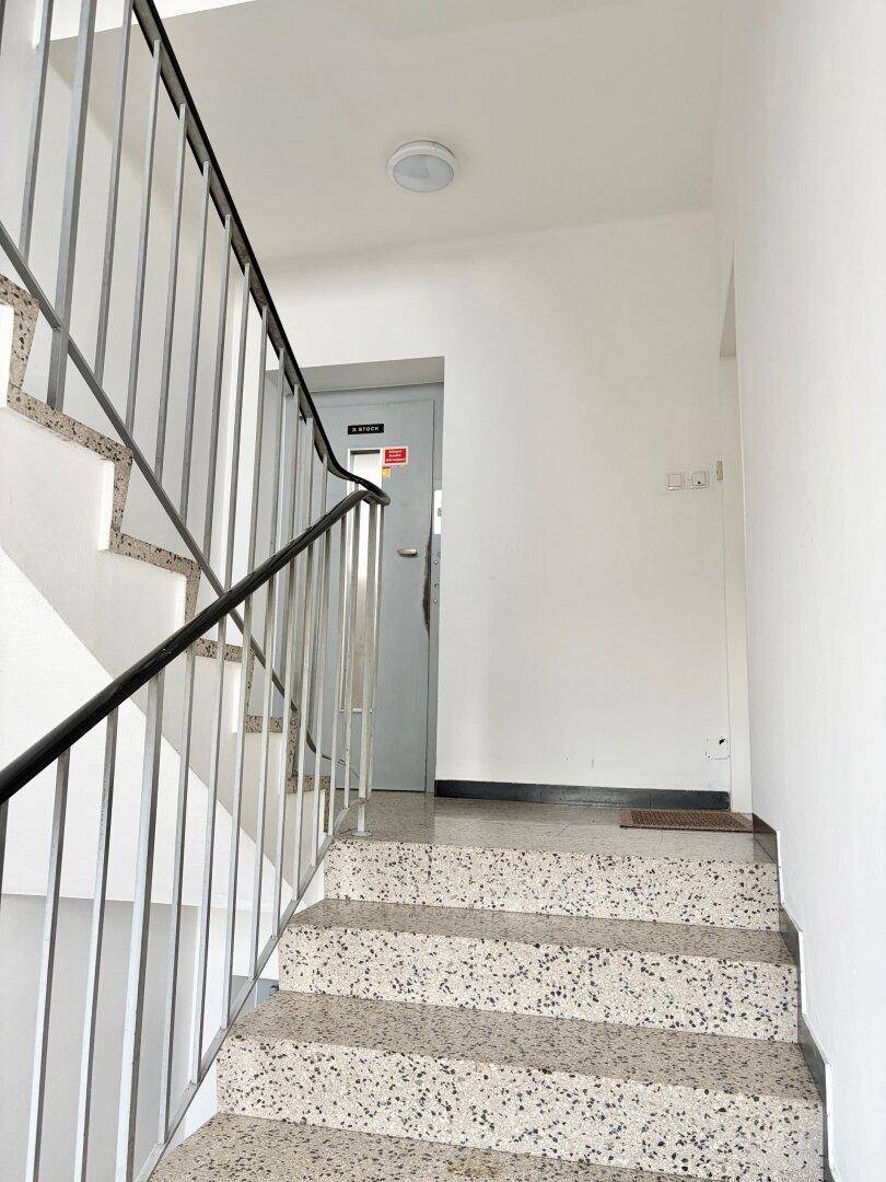 Helles Treppenhaus mit Terrazzoboden und schlichtem Metallgeländer in einem Mehrfamilienhaus.