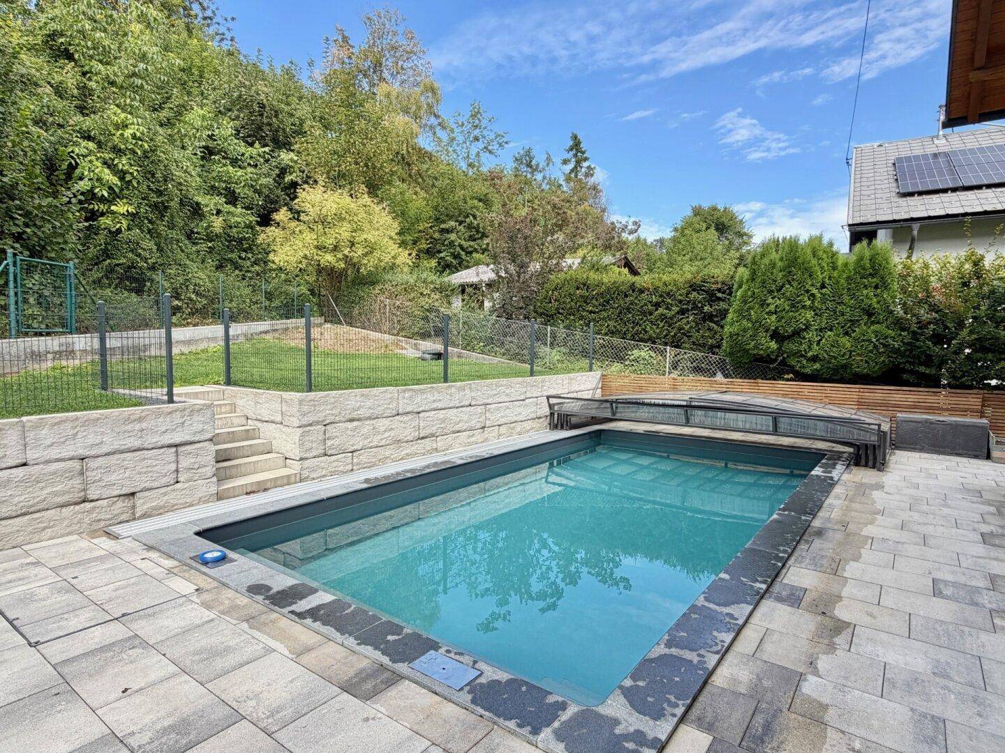 Moderner Außenpool mit gepflasterter Terrasse und umgebender Natur, ideal zum Entspannen.