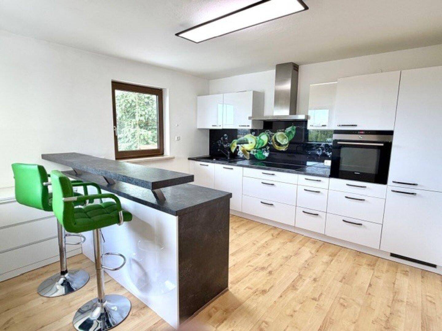 Moderne Küche mit weißen Hochglanzfronten, schwarzer Arbeitsplatte und einer Frühstücksbar mit Barhockern.