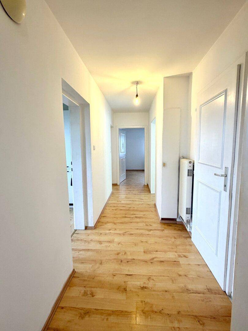 Heller Flur mit Laminatboden und weißen Wänden, der zu weiteren Räumen führt.