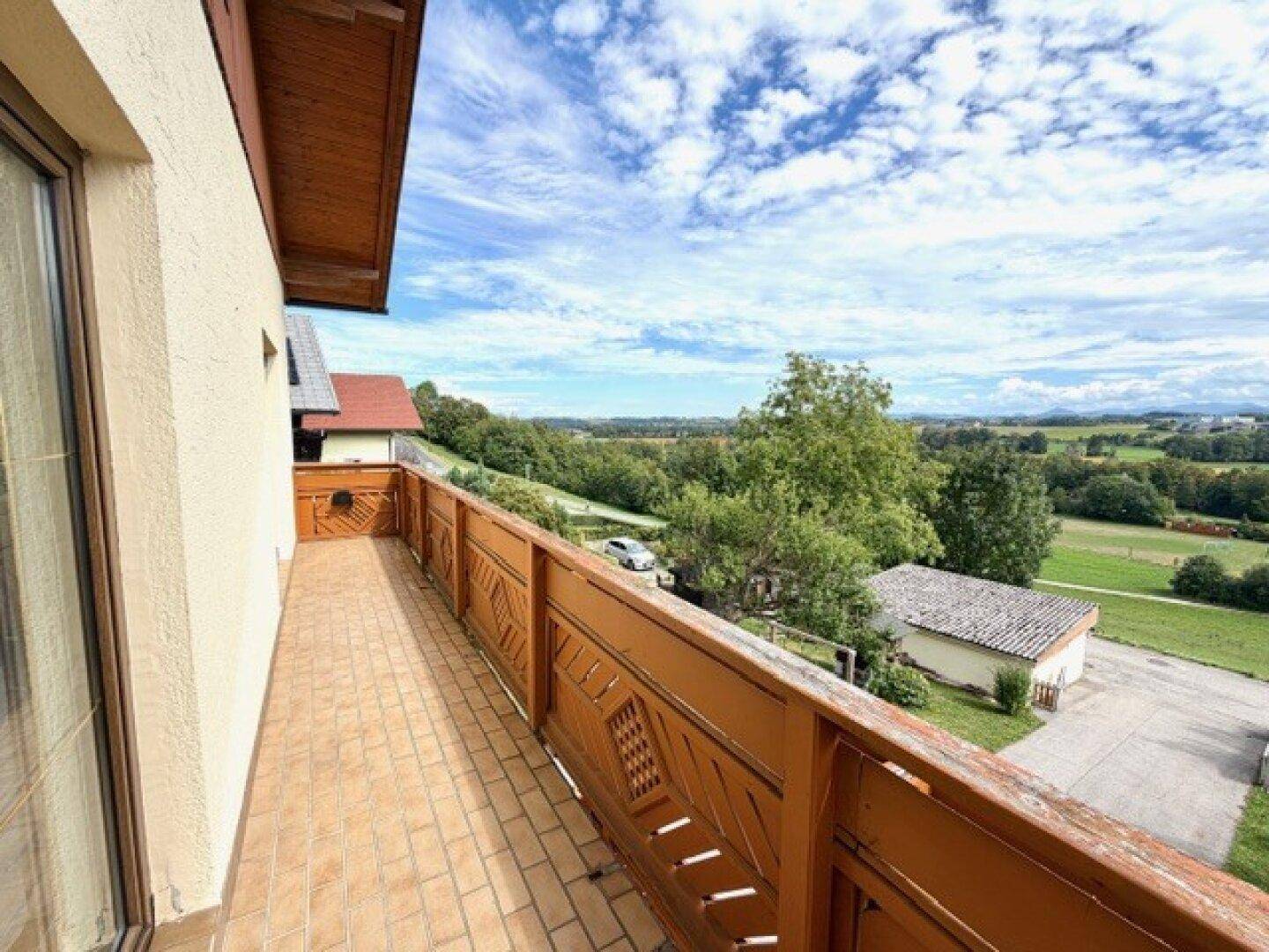 Geräumiger Balkon mit Terrakotta-Fliesen und Holzgeländer, bietet einen weiten Blick ins Grüne.