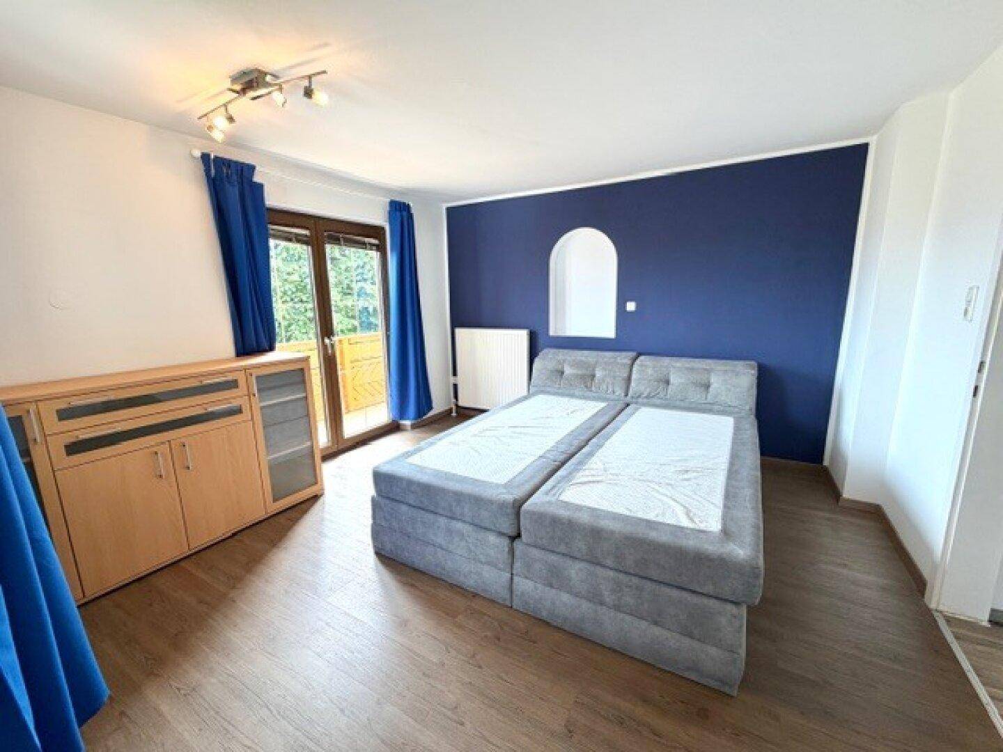 Schlafzimmer mit blauer Akzentwand, bequemem Bett und direktem Zugang zum Balkon.