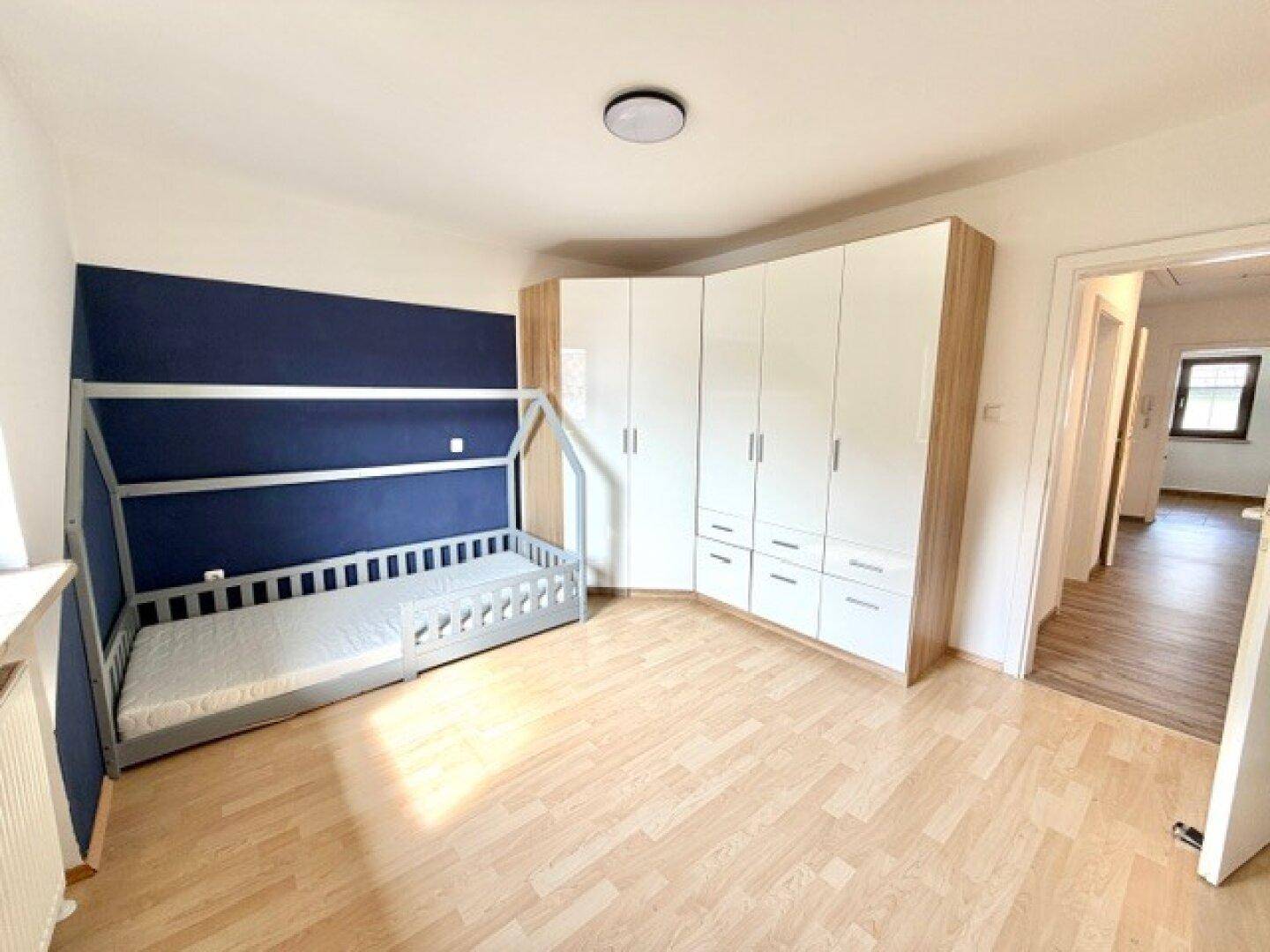 Kinderzimmer mit Hausbett, blauer Akzentwand und praktischen Eckkleiderschränken.