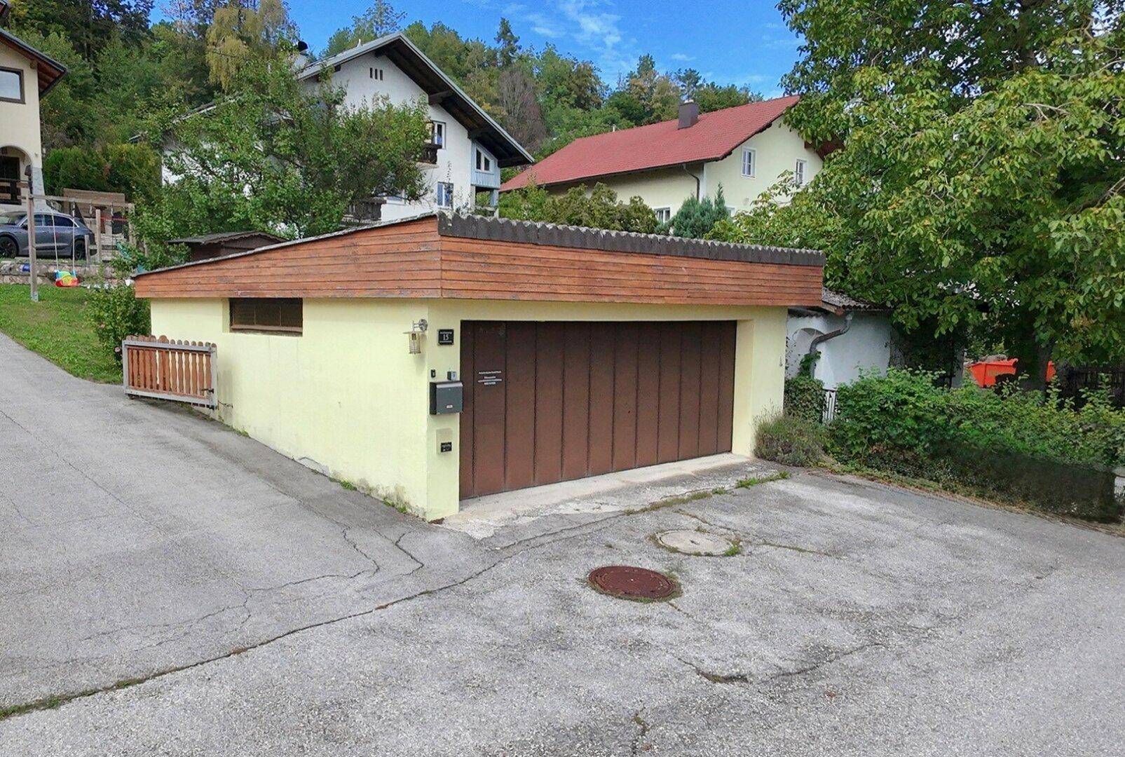 Separate Garage mit braunem Tor und Holzverkleidung, bietet zusätzlichen Stauraum.