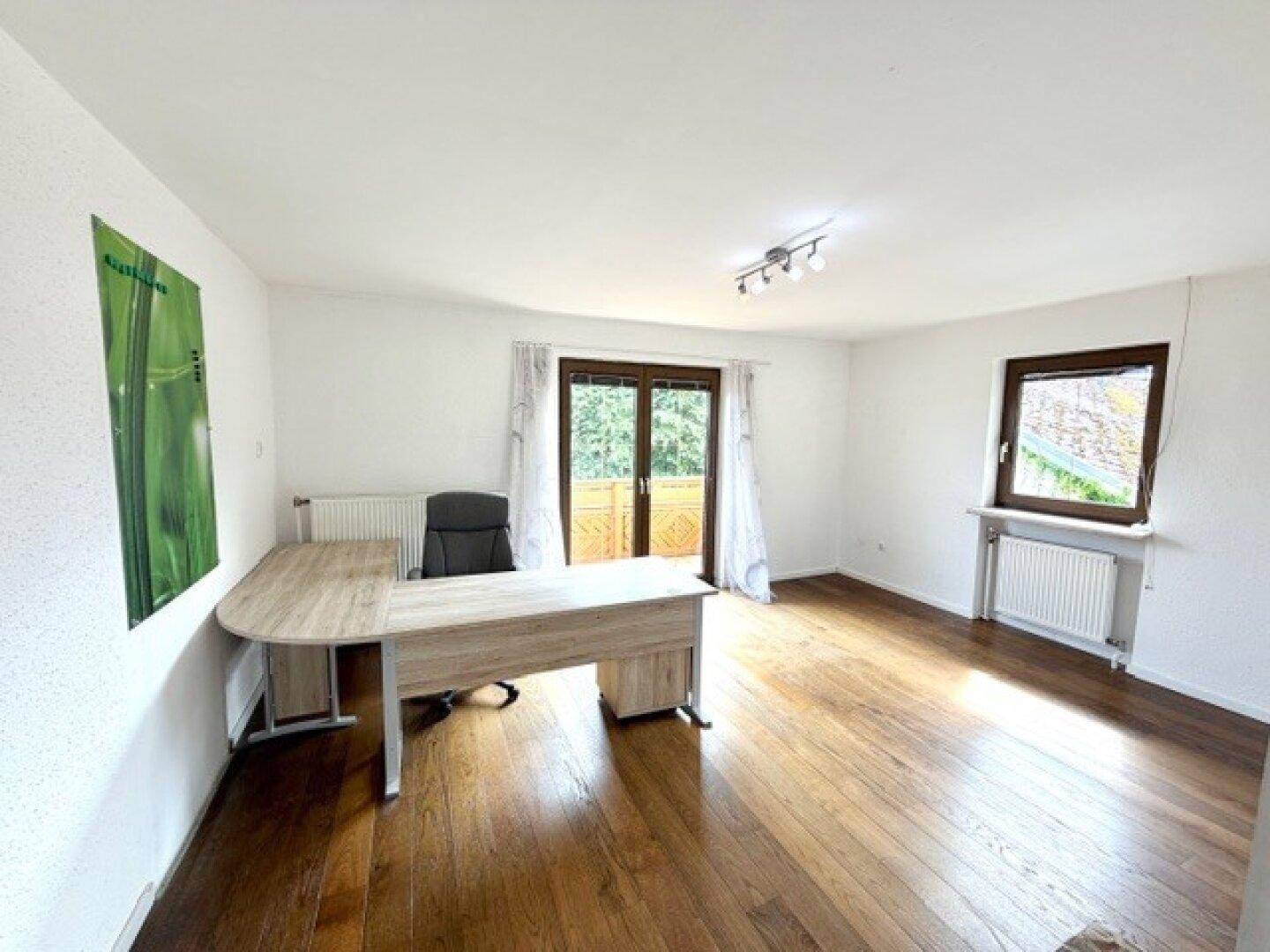 Helles Arbeitszimmer mit Holzschreibtisch, Parkettboden und Zugang zu einem Balkon.