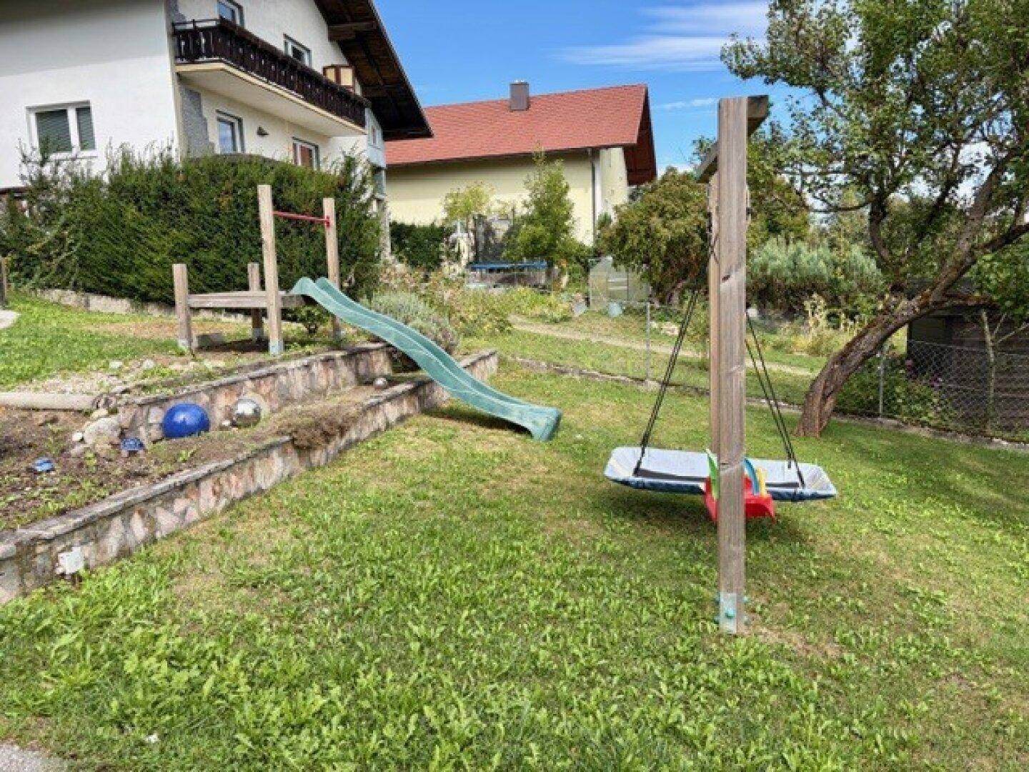Spielbereich im Garten mit Rutsche und Schaukel, ideal für Kinder im Freien.