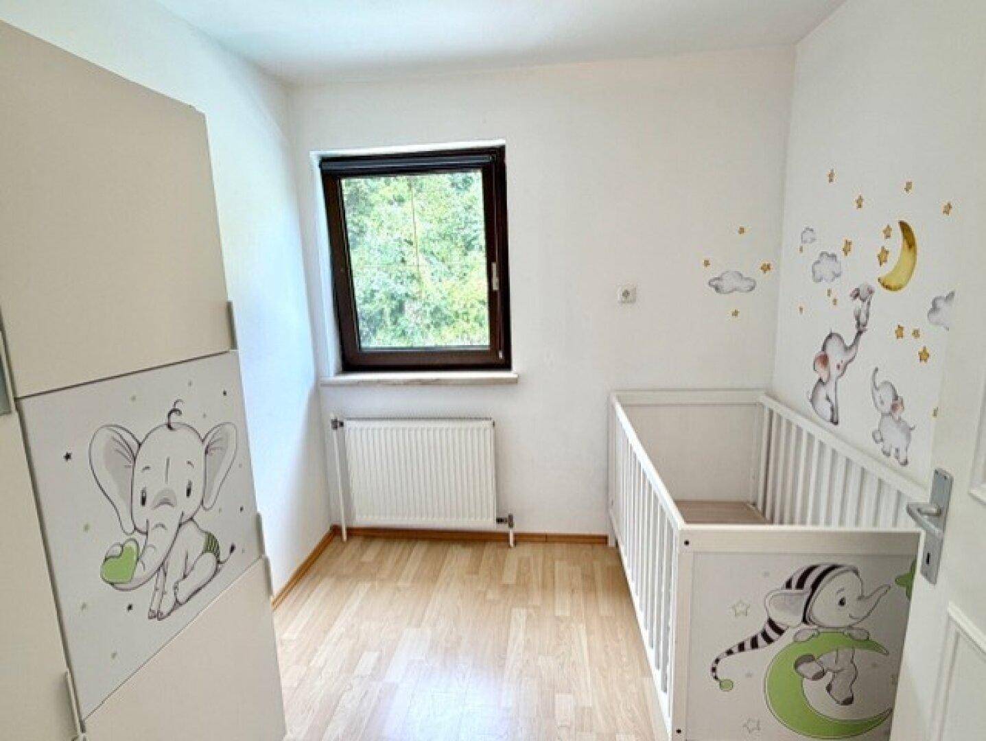 Helles Kinderzimmer mit Babybett, Fenster und niedlichen Elefanten-Wandstickern.