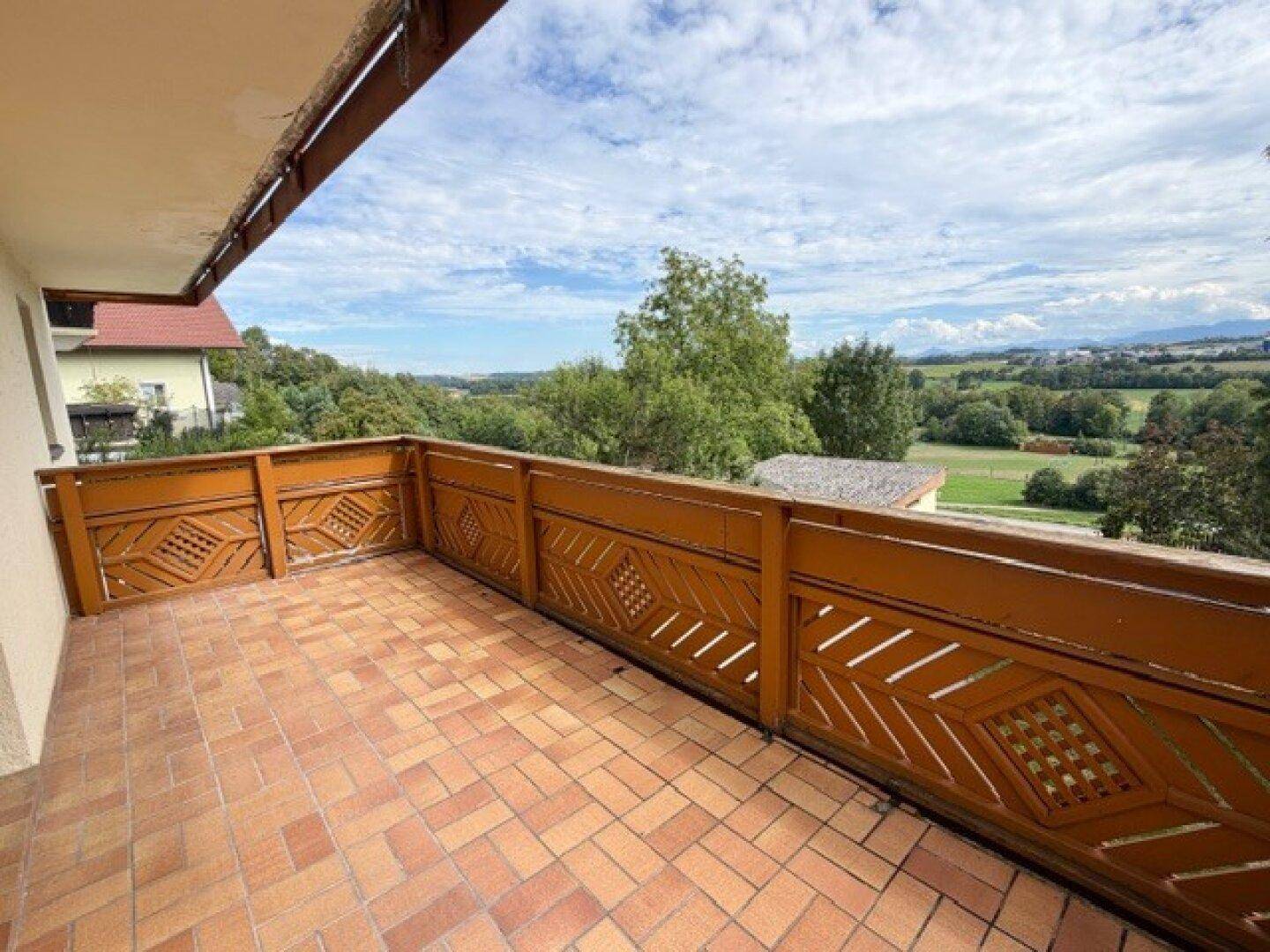 Geräumiger Balkon mit Terrakotta-Fliesen und Holzgeländer, bietet einen weiten Blick ins Grüne.