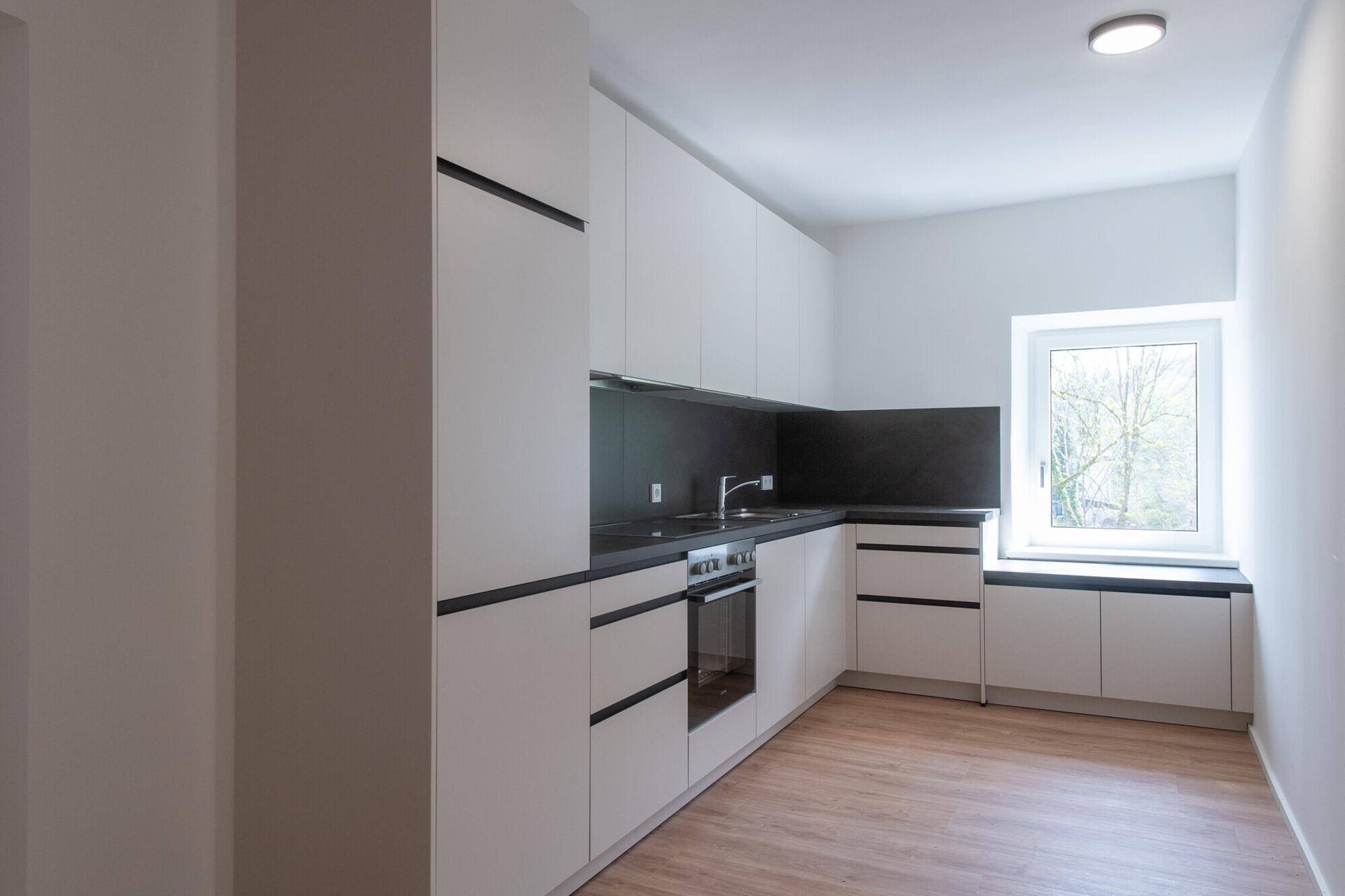 Funktionale Einbauküche mit weißen Fronten, integrierten Geräten und einem Fenster.