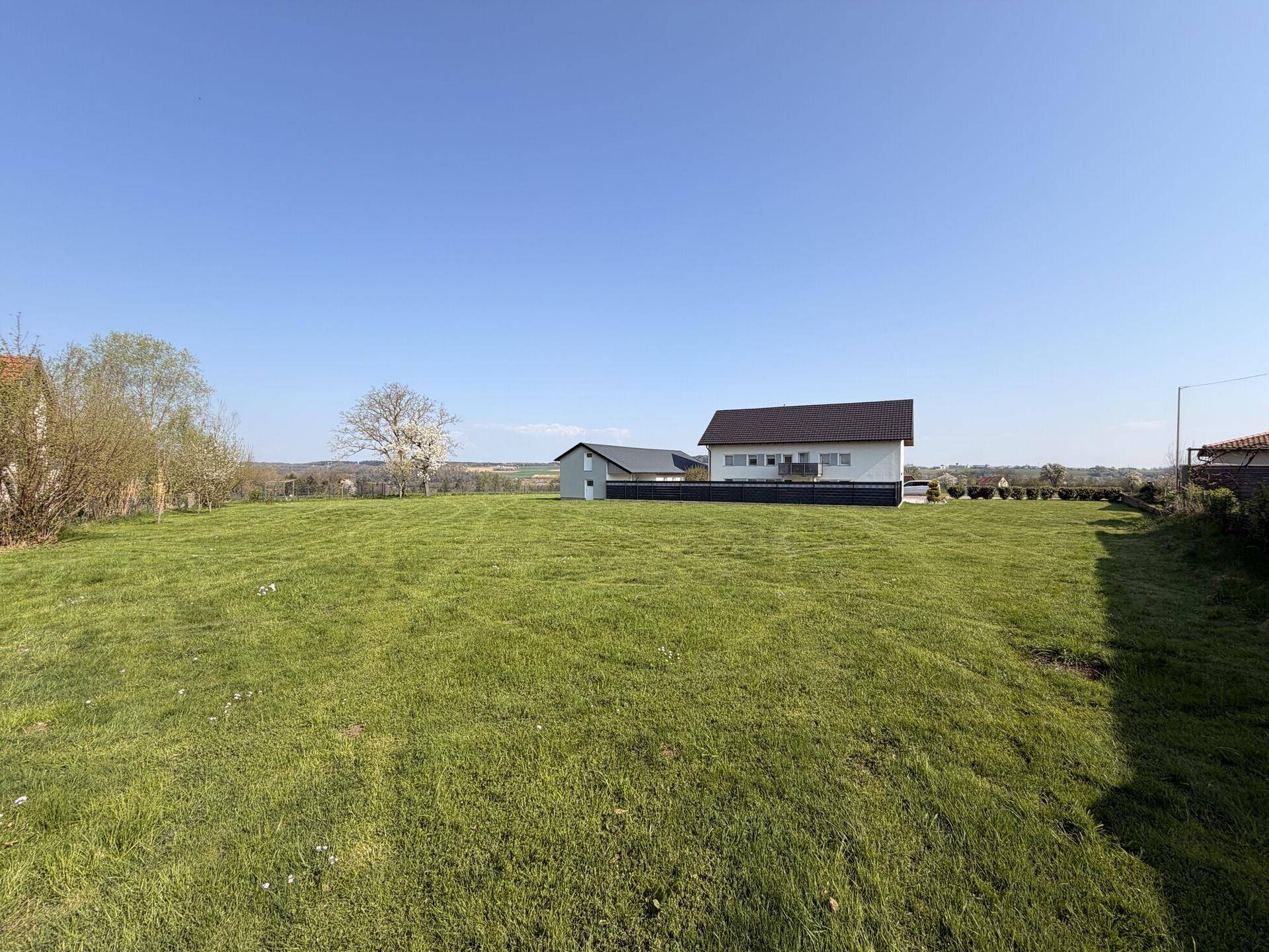 Offene grüne Fläche mit einem modernen Haus im Hintergrund und weitem Blick in die Landschaft.