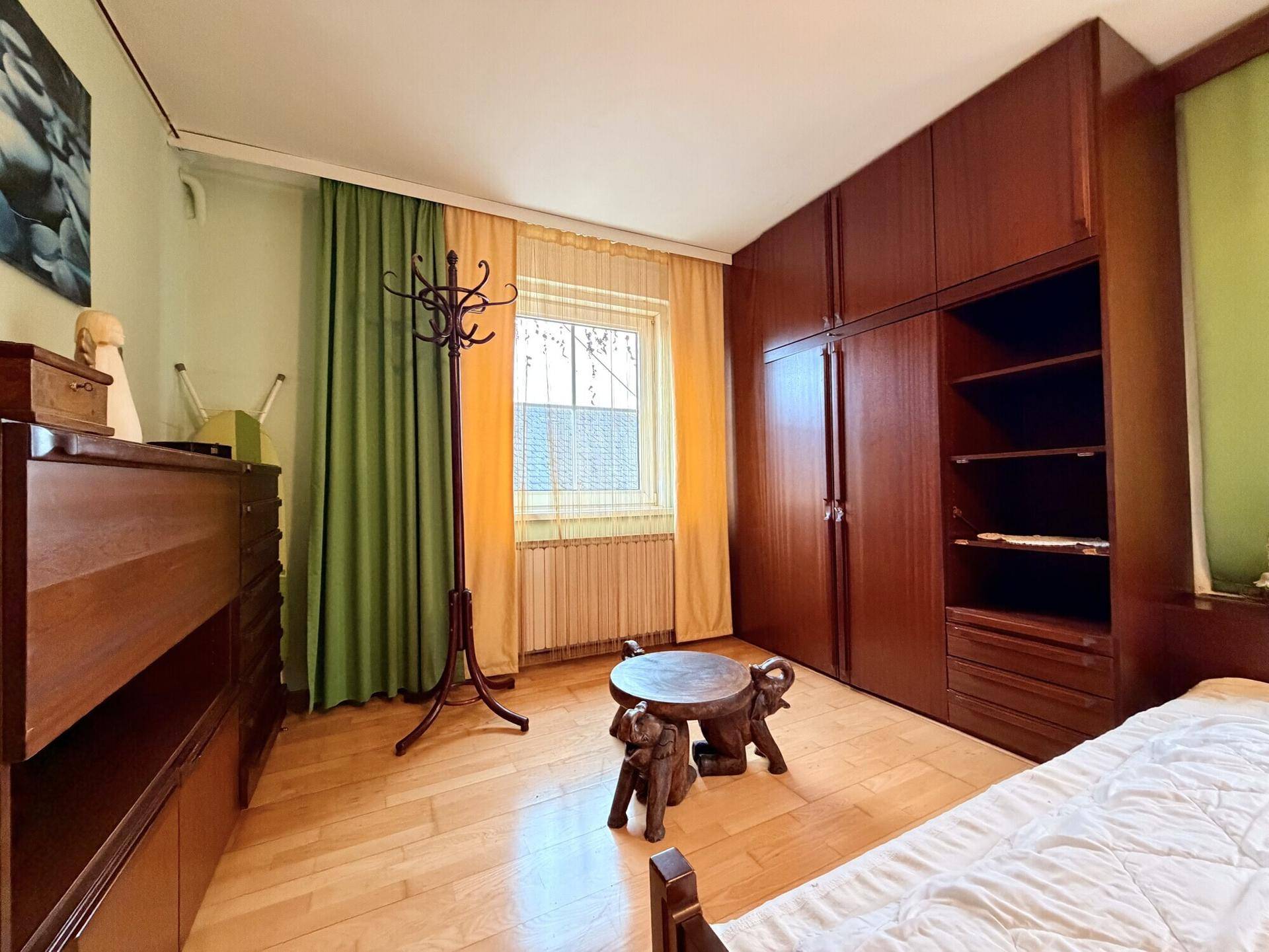 Helles Schlafzimmer mit Holzboden, Einbauschränken und einem Fenster mit Blick ins Grüne.